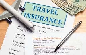 Travel insurance documents with a toy airplane, pen, booking confirmation, and US dollar bills.