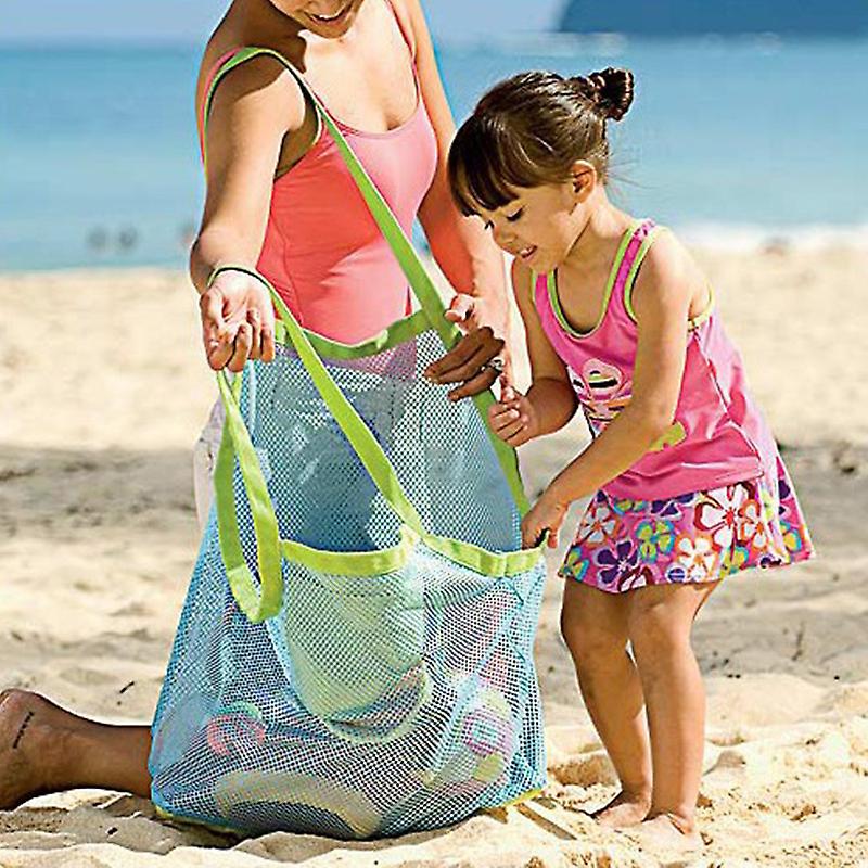 Woman and child holding a mesh beach bag filled with toys on a sandy beach.