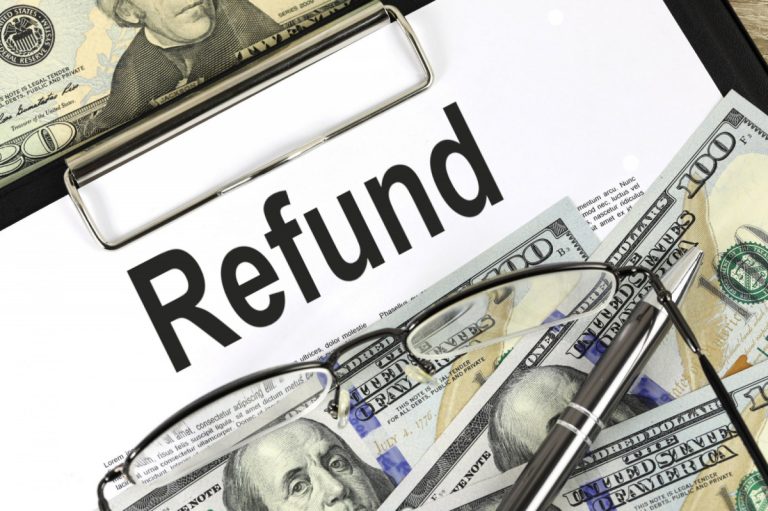 A "Refund" document on a clipboard surrounded by US dollar bills, a pair of glasses, and a silver pen.
